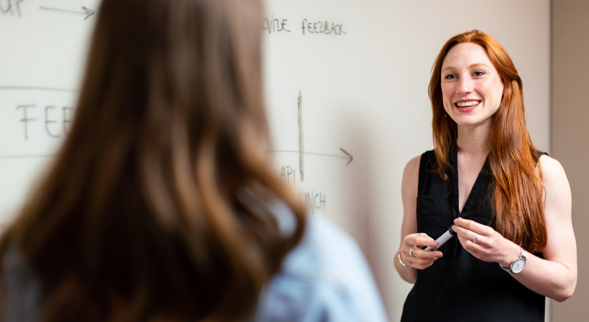 Women presenting work on a whiteboard to another