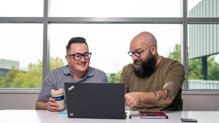 Two men sitting at a desk with a laptop
